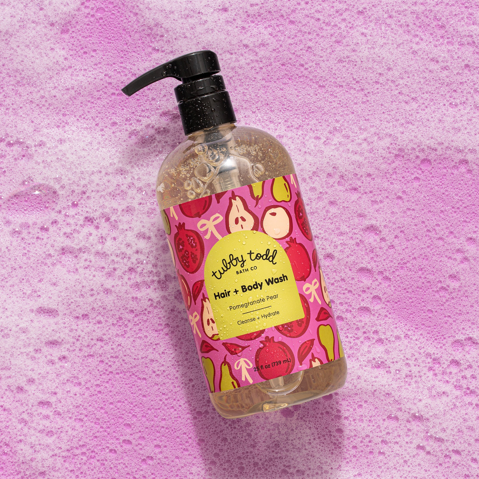 Pom Pear Hair + Body Wash 25oz bottle lying on the pink color background within the bubbles.